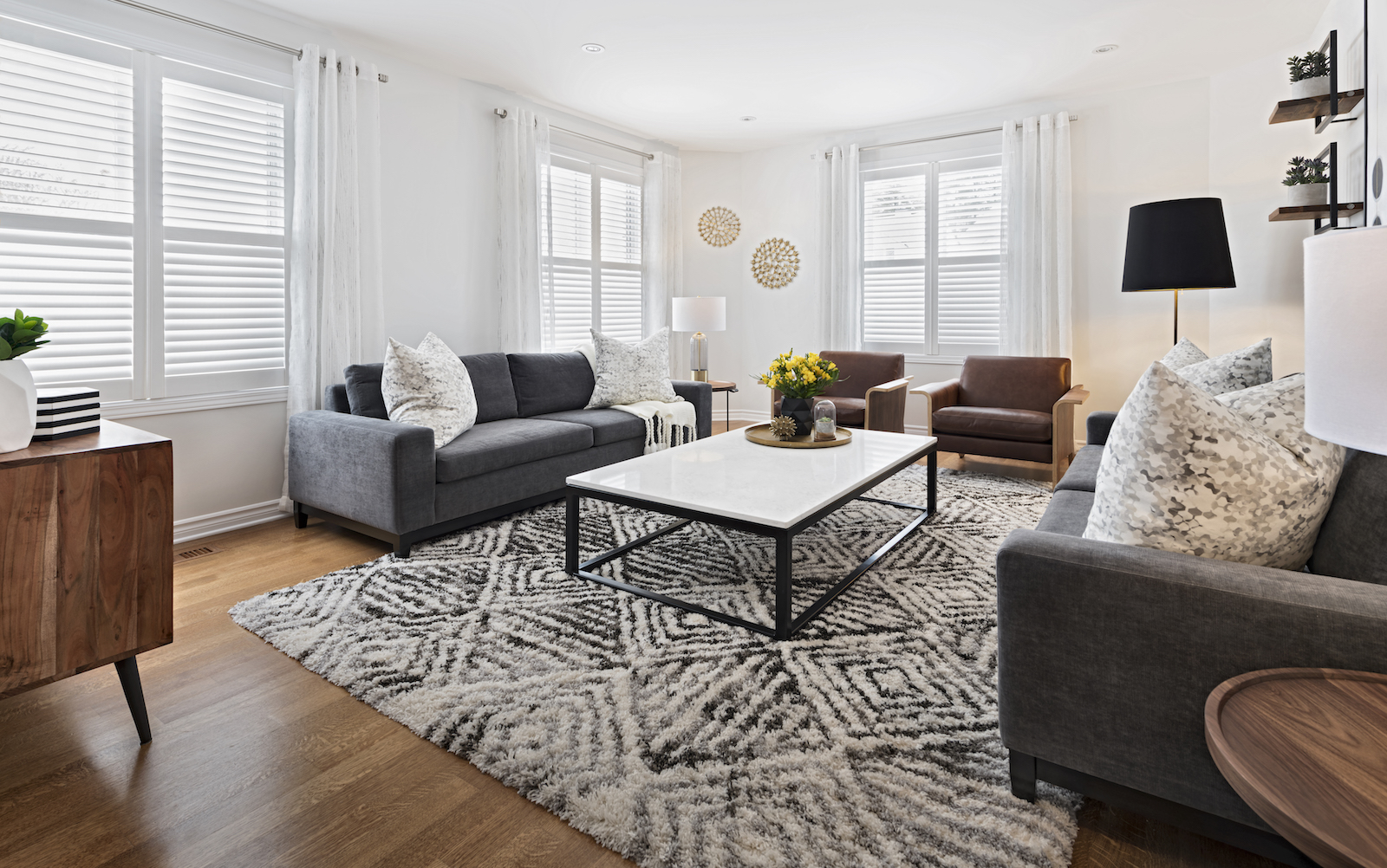 Modern living room in Ottawa designed by an interior decorator, featuring charcoal grey sofas, saddle tan leather chairs, white coffee table, geometric rug, and natural wood accents.