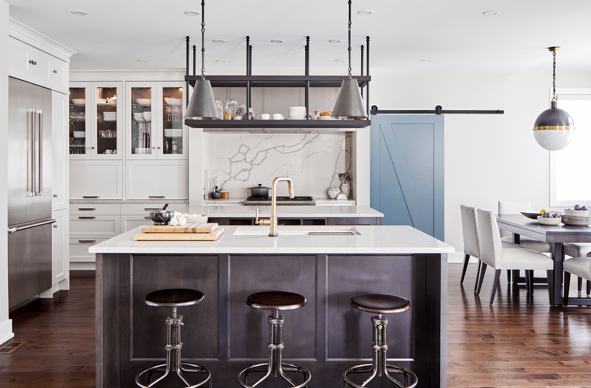 Transitional kitchen with dual islands, custom stainless steel hood fan, veined quartz backsplash, and industrial hanging shelving. Features dark wood island, built-in refrigerator, and custom cabinetry. Designed by Ottawa kitchen designers.